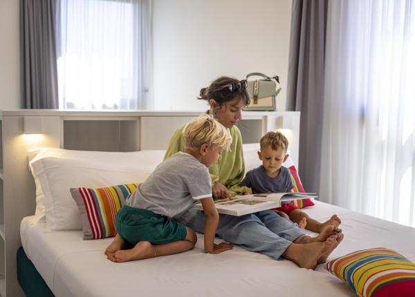 Woman reading a book with two children on a bed.